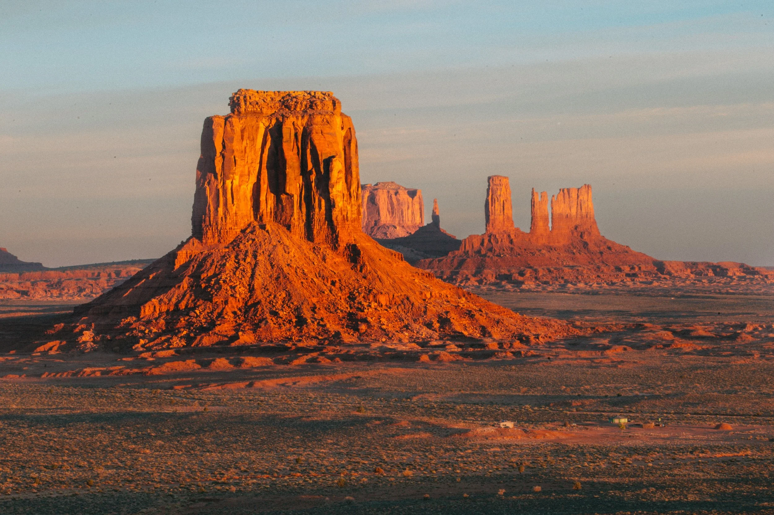 Sunset view of Monument Valley with large sandstone buttes illuminated in orange and pink sunset colors.