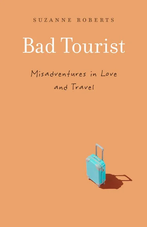 Book cover for "Bad Tourist" by Suzanne Roberts, with the subtitle "Misadventures in Love and Travel," featuring a small blue suitcase with a shadow on a peach background. Book & Author Publicity by Quatrain PR.