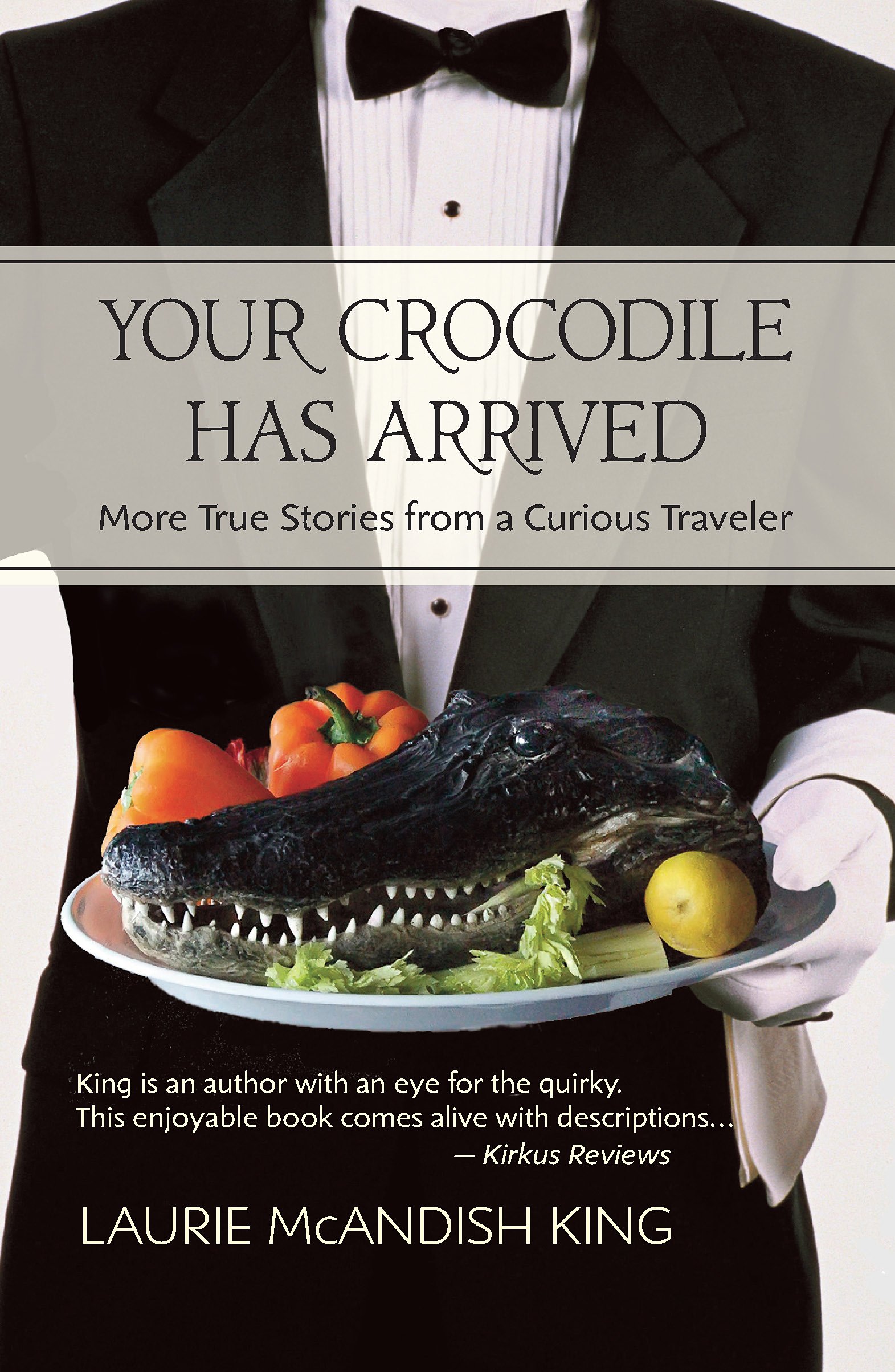 Book cover titled "Your Crocodile Has Arrived: More True Stories from a Curious Traveler" by Laurie McAndish King. The cover features a person in a tuxedo holding a plate with a crocodile-shaped food, orange bell peppers, and a lemon. Book & Author P