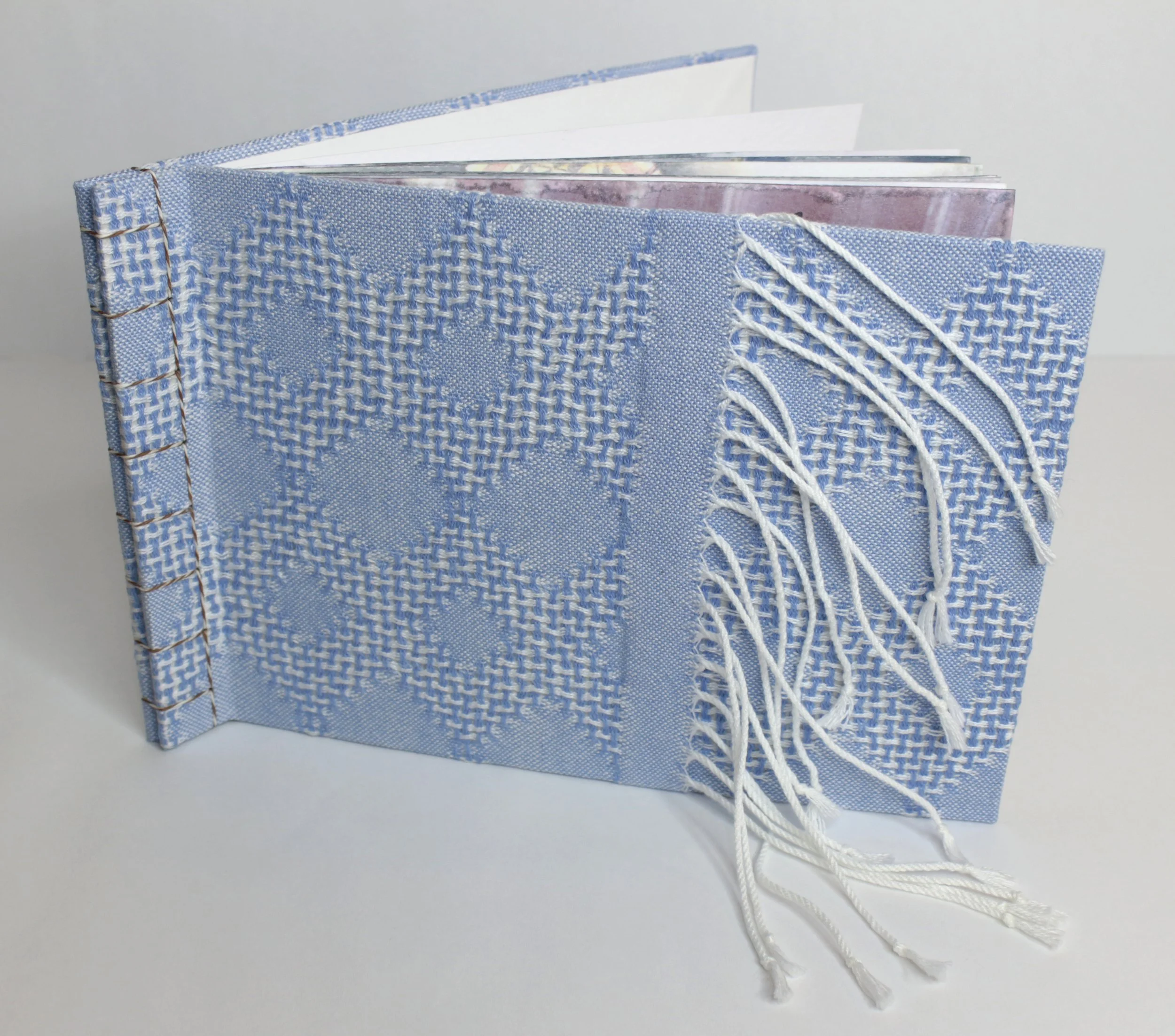A blue embroidered book cover with white thread, featuring geometric and floral patterns, with pages inside.