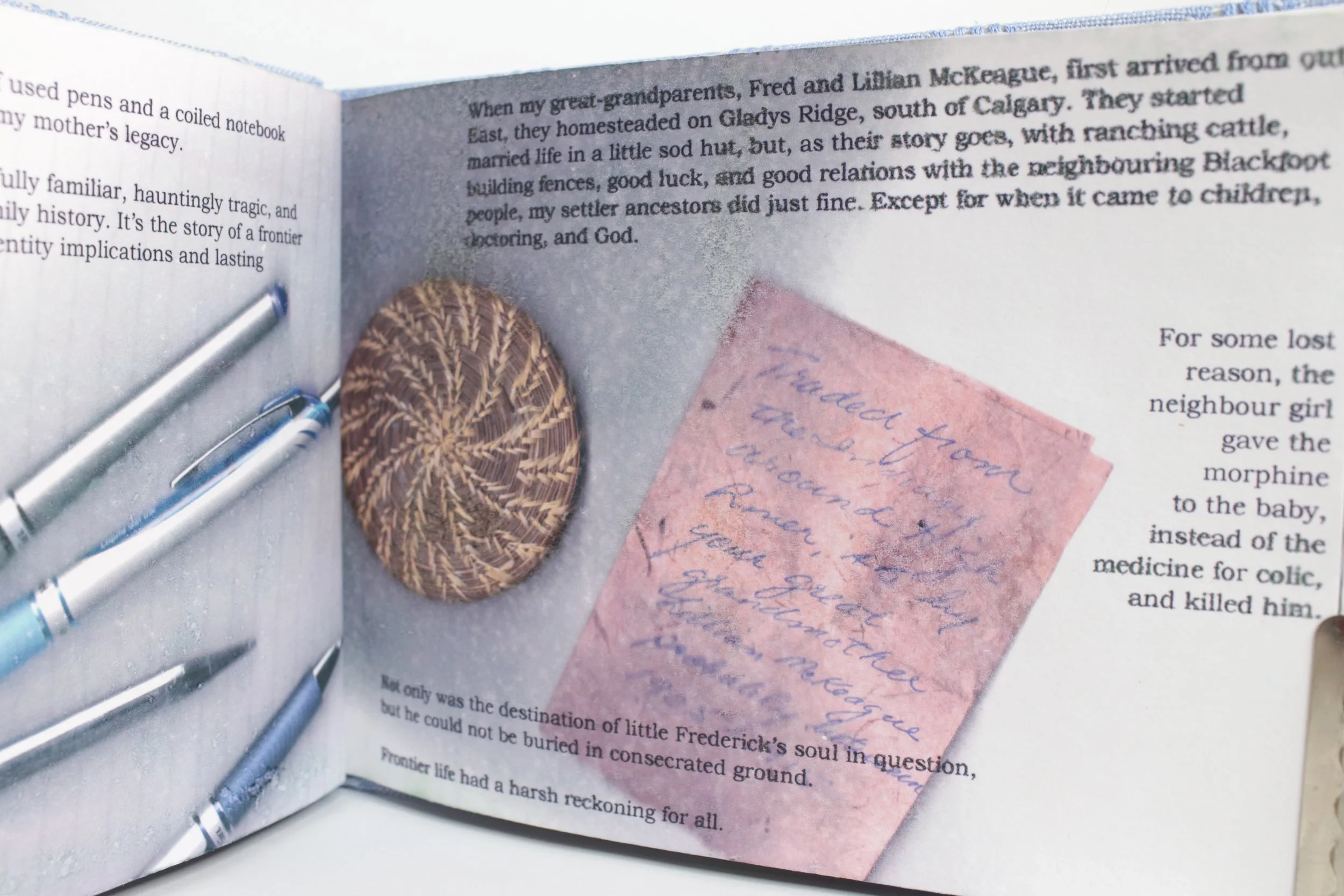 An open book with a pink handwritten note, a carved wooden oval object, and three silver pens placed on the page.