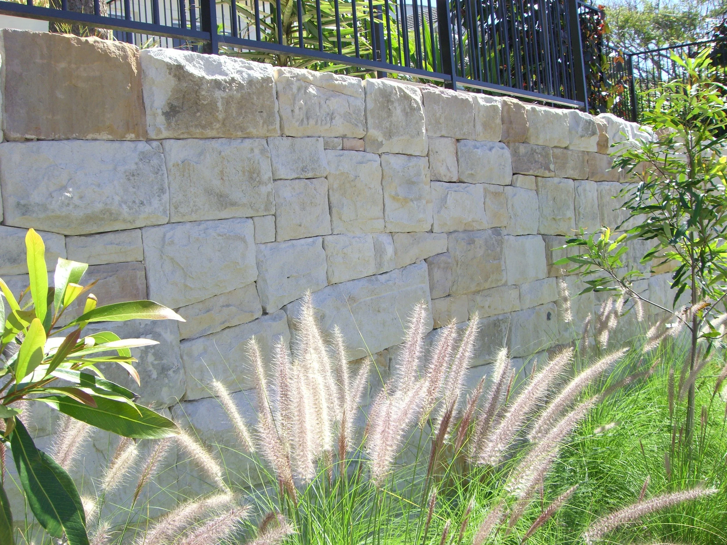Light sandstone boundary wall integrating fence and retaining, softened by greenery
