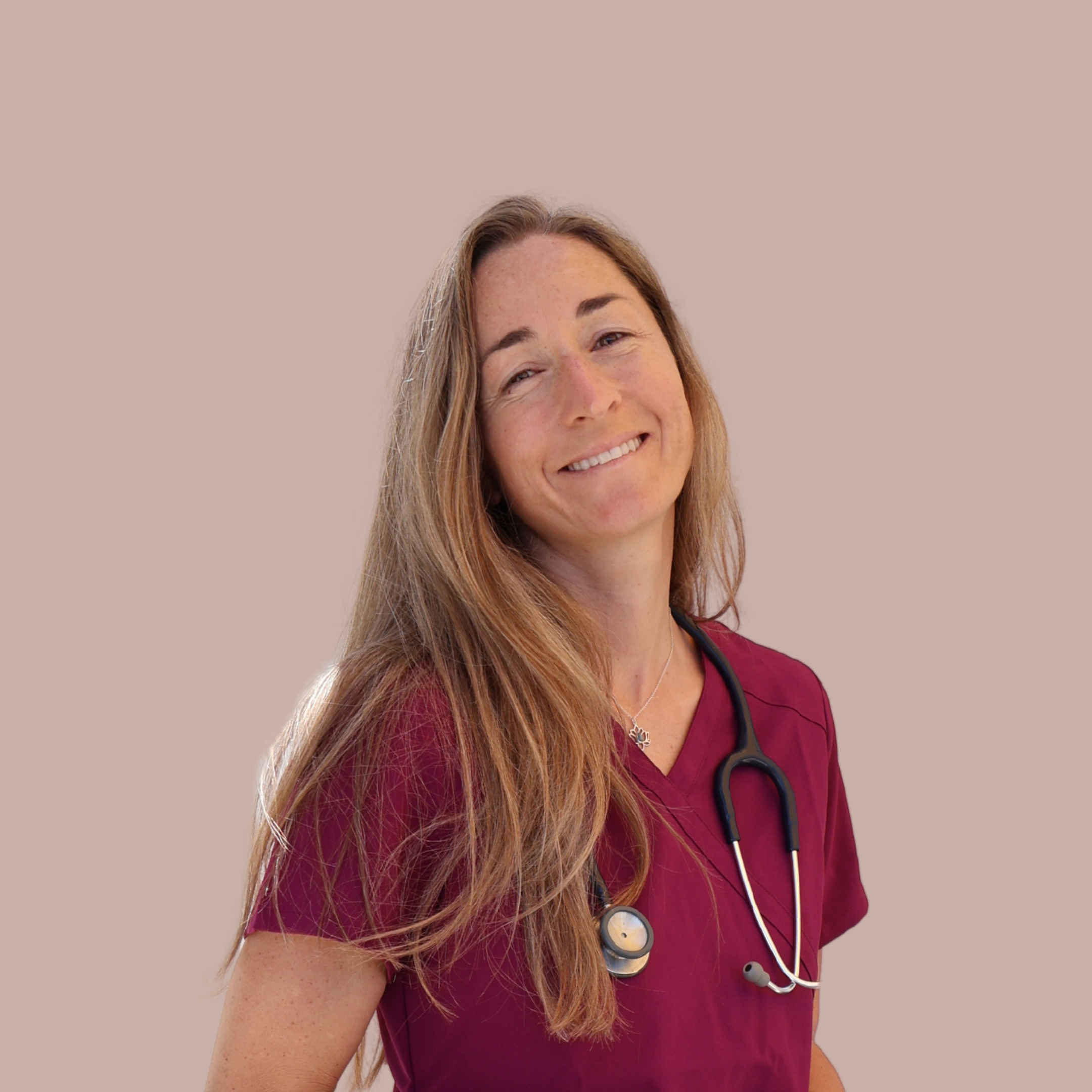 A woman with long, wavy, reddish-brown hair, wearing maroon scrubs and a stethoscope around her neck, smiling warmly.