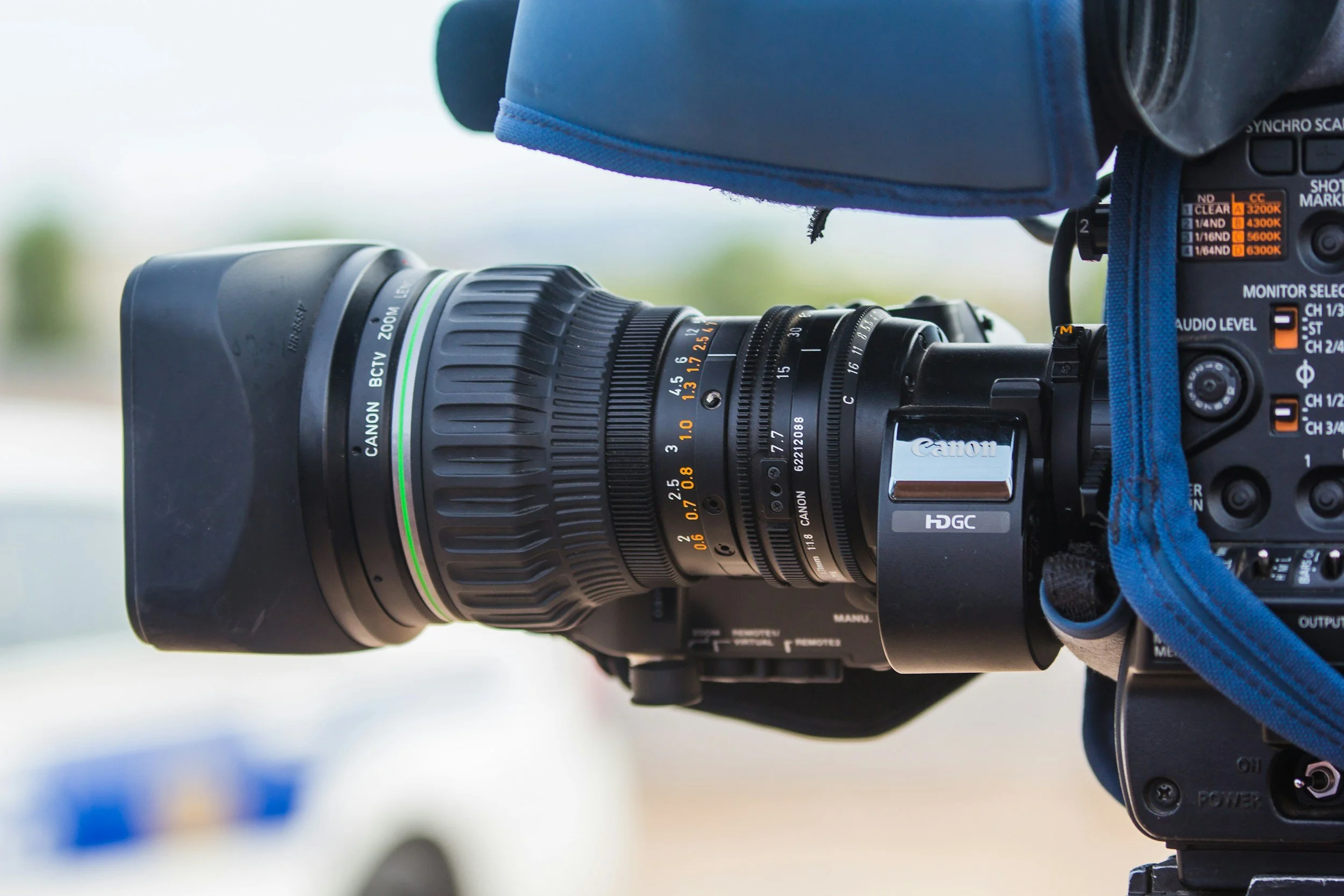 Close-up of a professional video camera with a large Canon lens and various control buttons and dials.