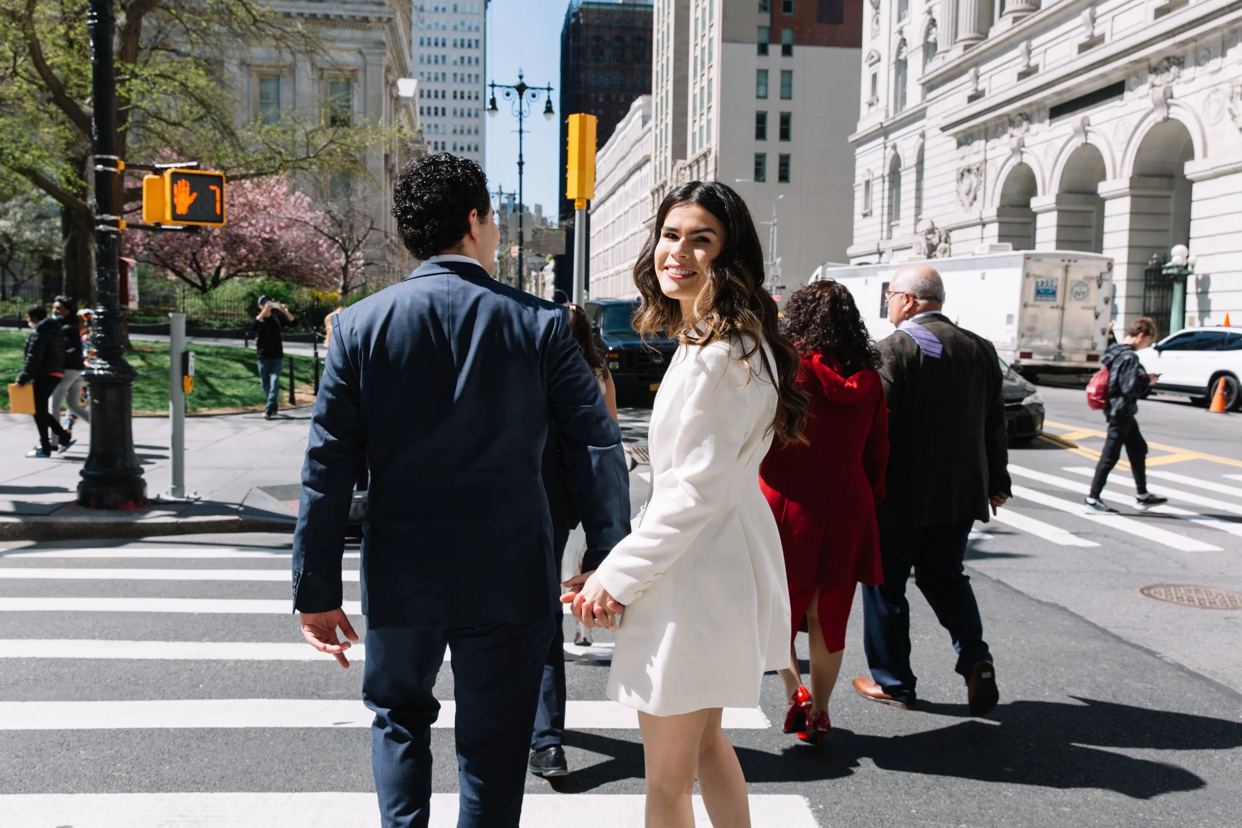 wedding bridge and groom walk through crosswalk in downtown manhattan for courthouse wedding ceremony