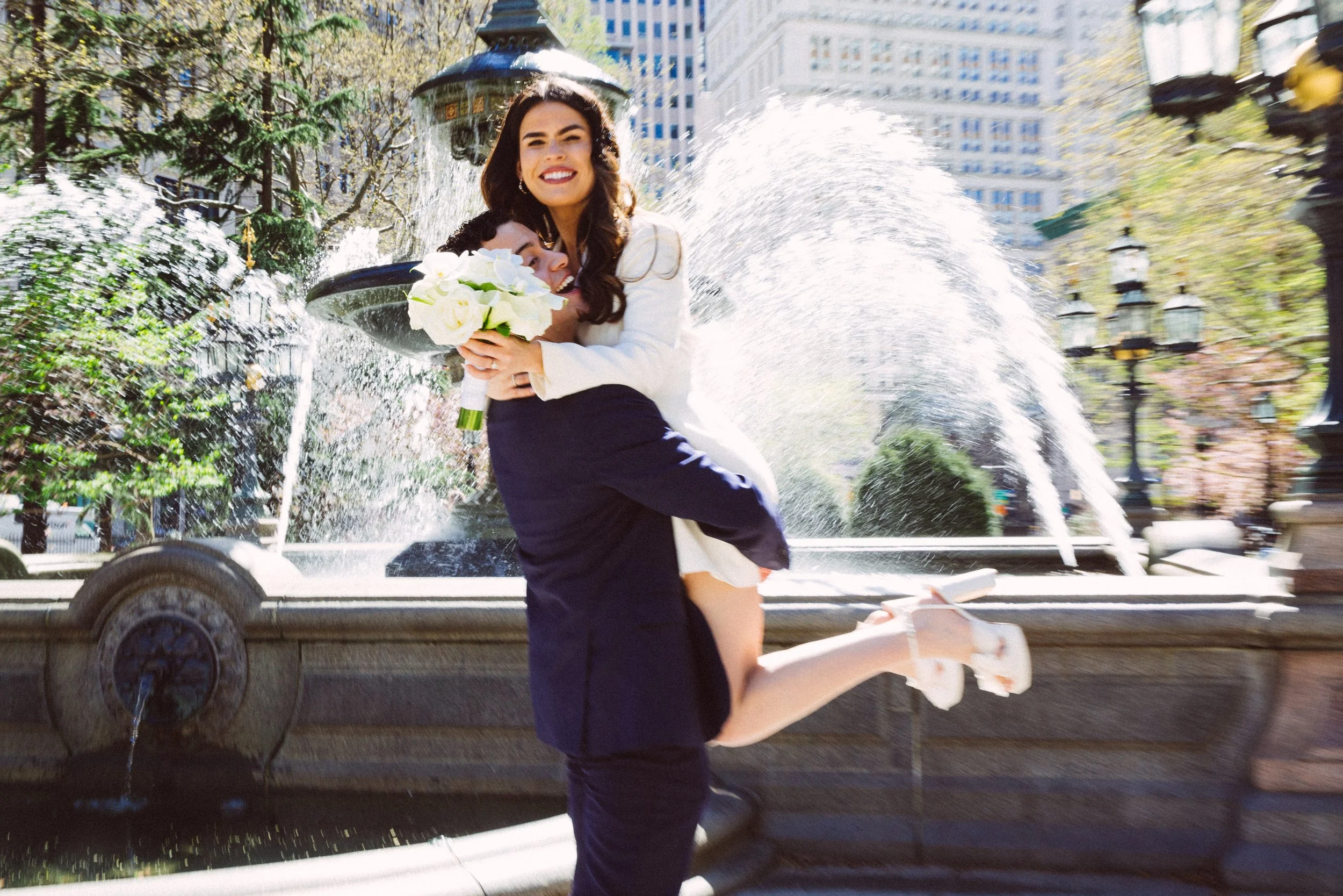 groom carrying bride in front of fountain at wedding in downtown manhattan nyc