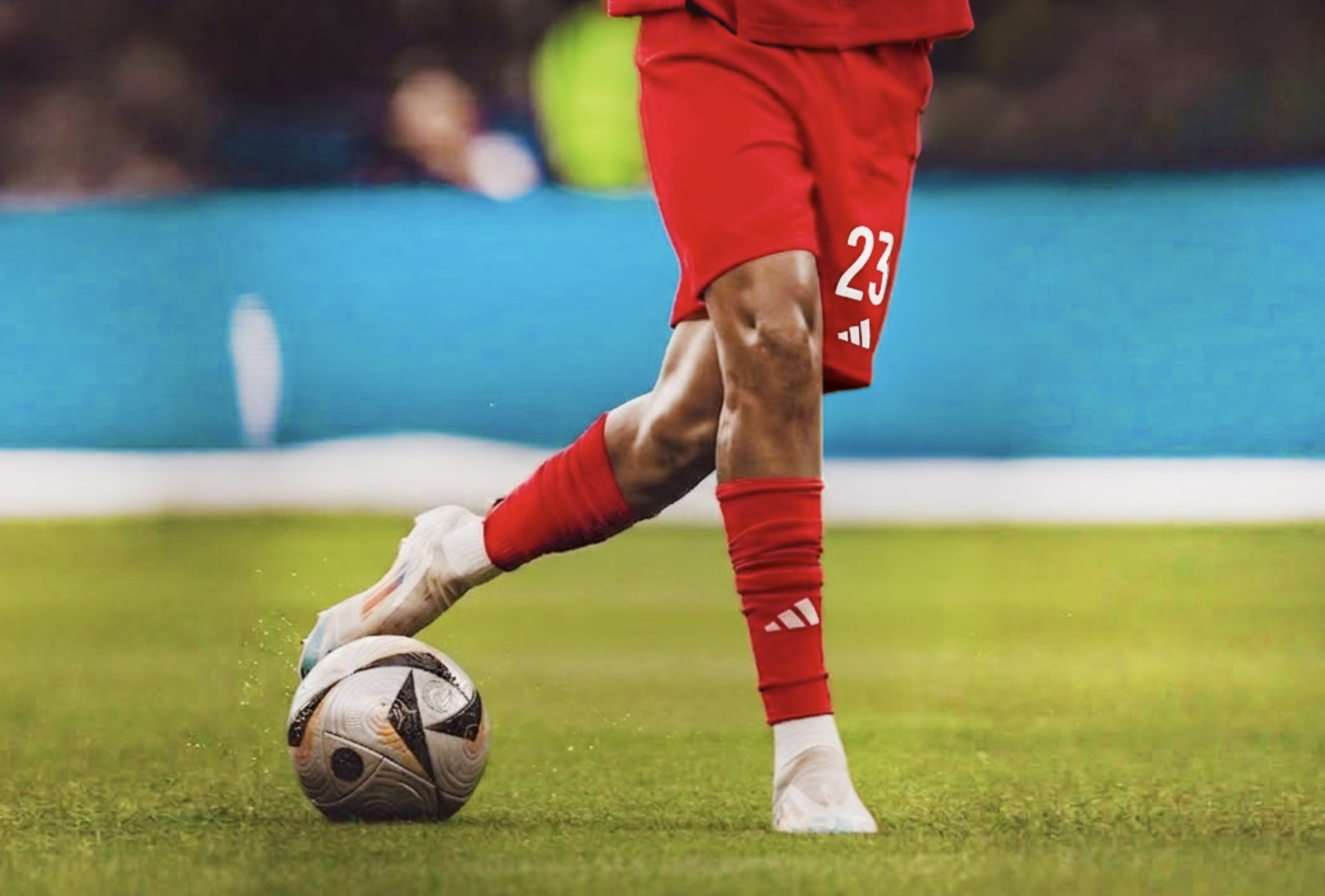 A soccer player wearing red shorts and red socks is kicking a soccer ball on a green field.
