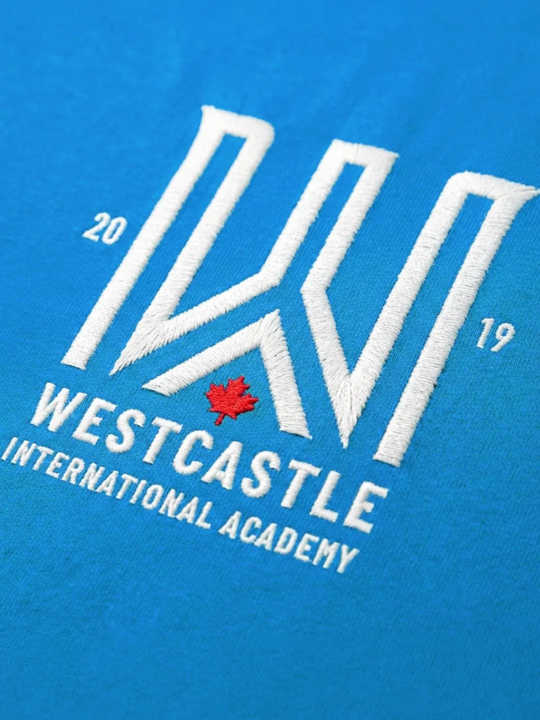 Embroidery of a logo for Westcastle International Academy on a blue fabric background, with the year 2019 and a red maple leaf