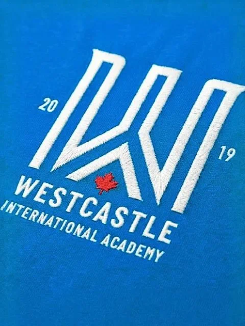 Logo of Westcastle International Academy with stylized 'W' and 'V' and a red maple leaf, on a blue background.