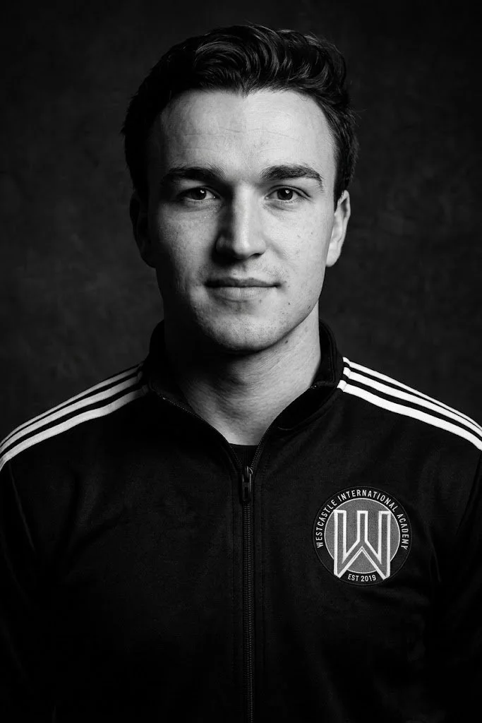 Black and white portrait of a young man wearing a sports jacket with the Westside International Academy logo.