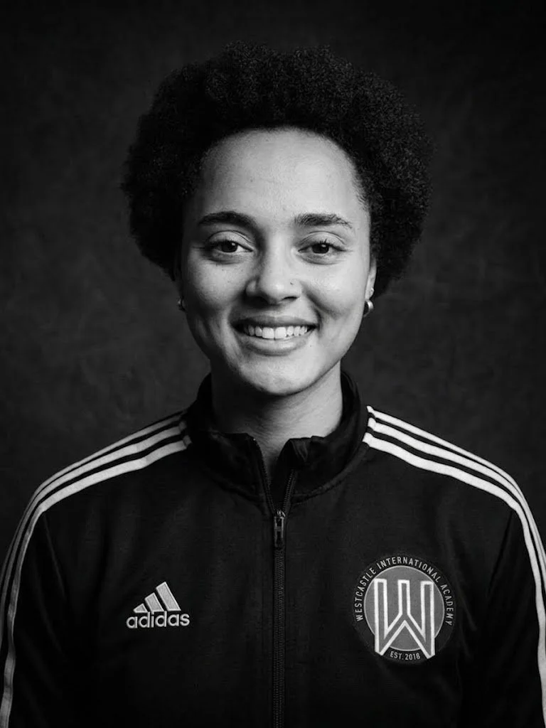 Black and white photo of a smiling woman with natural hair wearing an Adidas sports jacket with Westside International Academy logo on the chest.