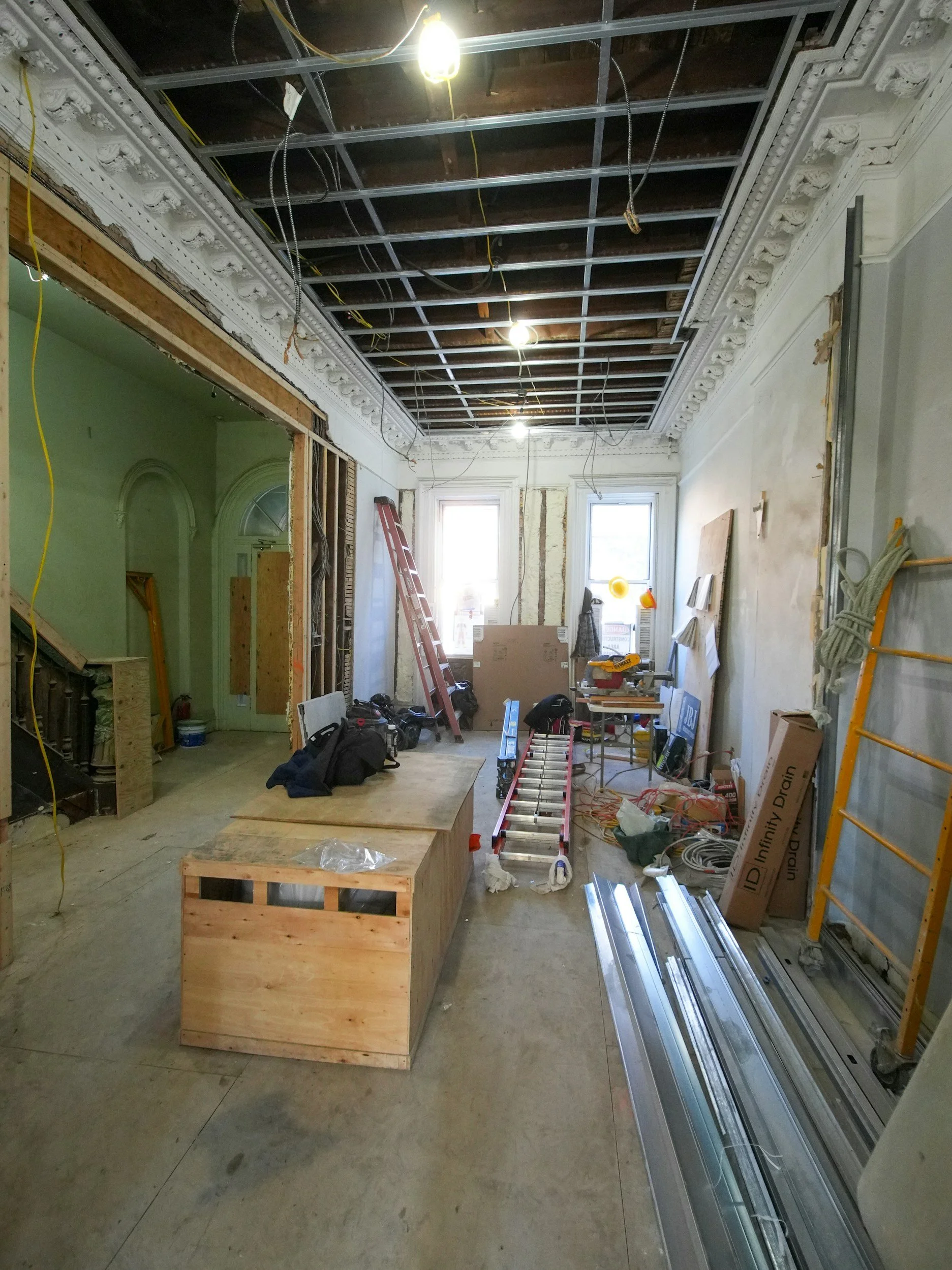 Interior of a building undergoing renovation with exposed ceiling framework, construction tools, and materials scattered around.