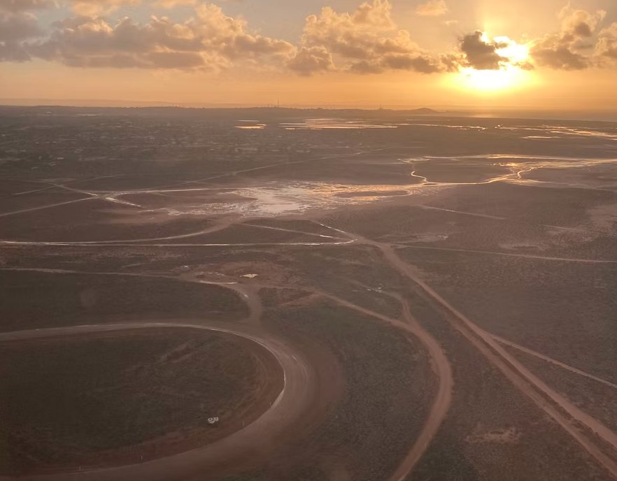 Aerial view of a landscape with dirt roads and water patches during sunset, cloudy sky in the background.