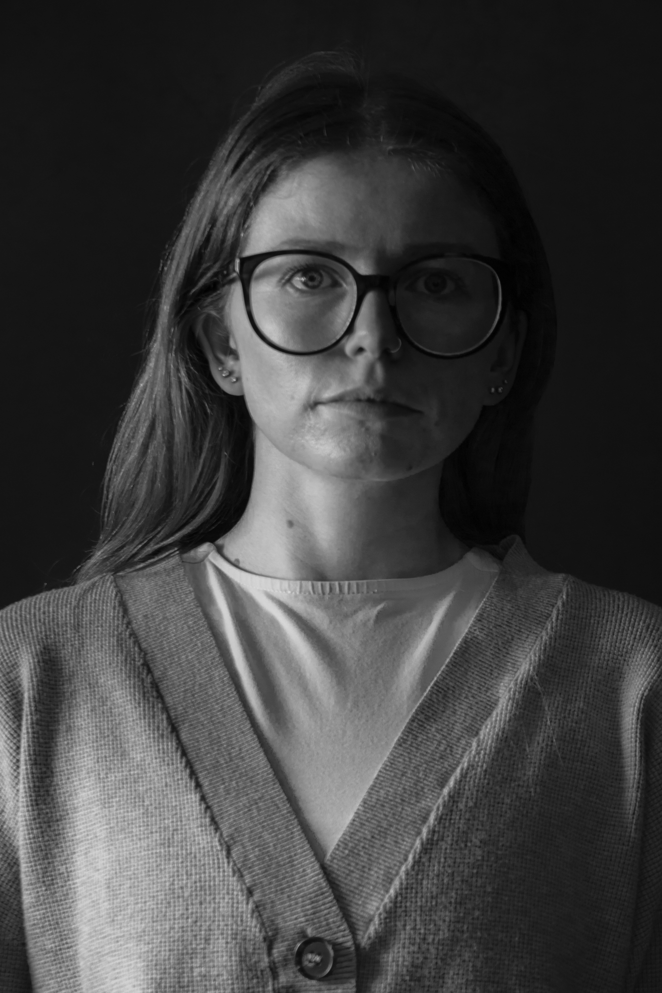 Black and white portrait of a woman with glasses, wearing a cardigan over a T-shirt, against a dark background.