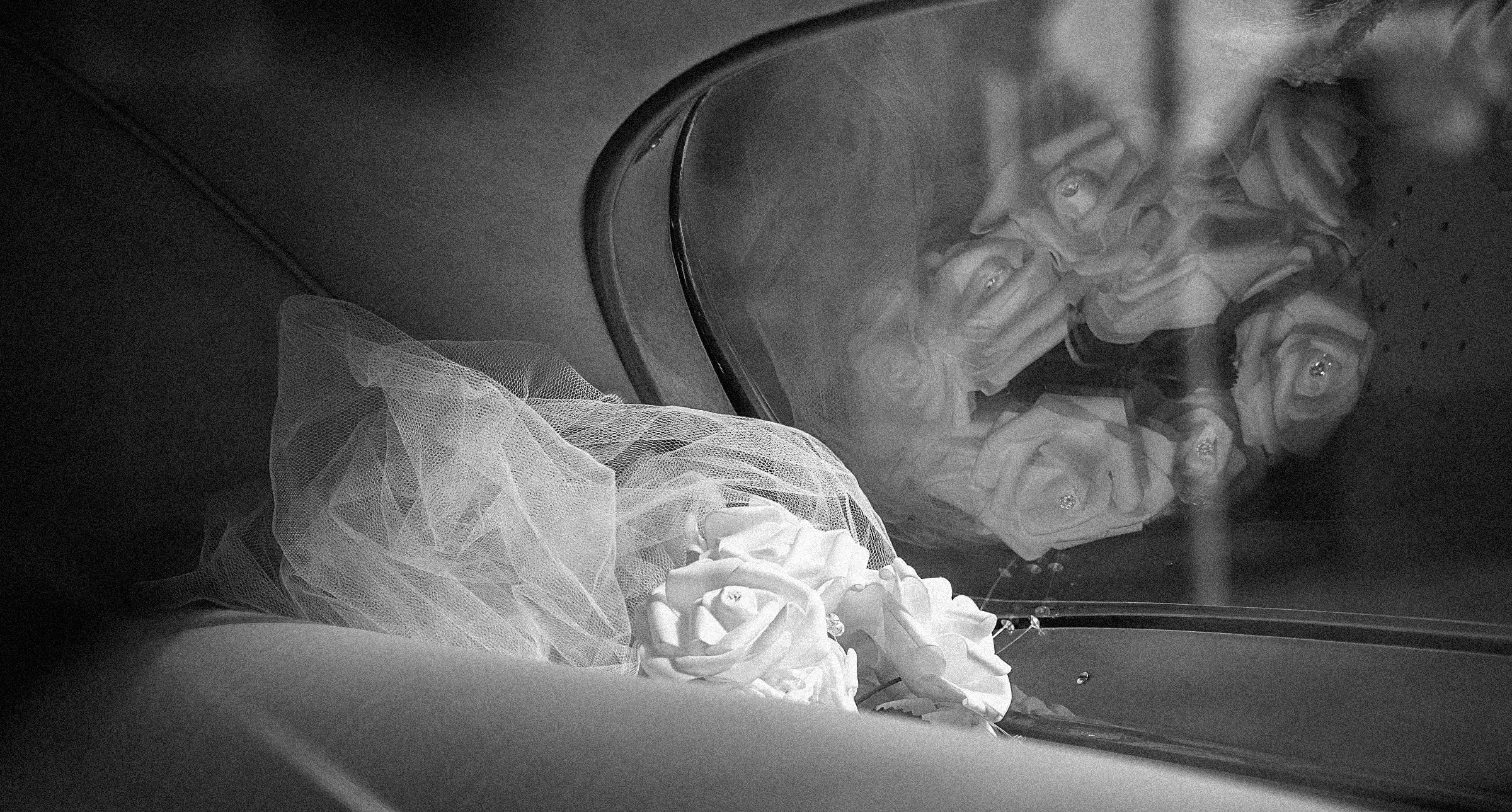 Black and white photo of a bouquet of roses and decorative fabric, reflected in a mirror.