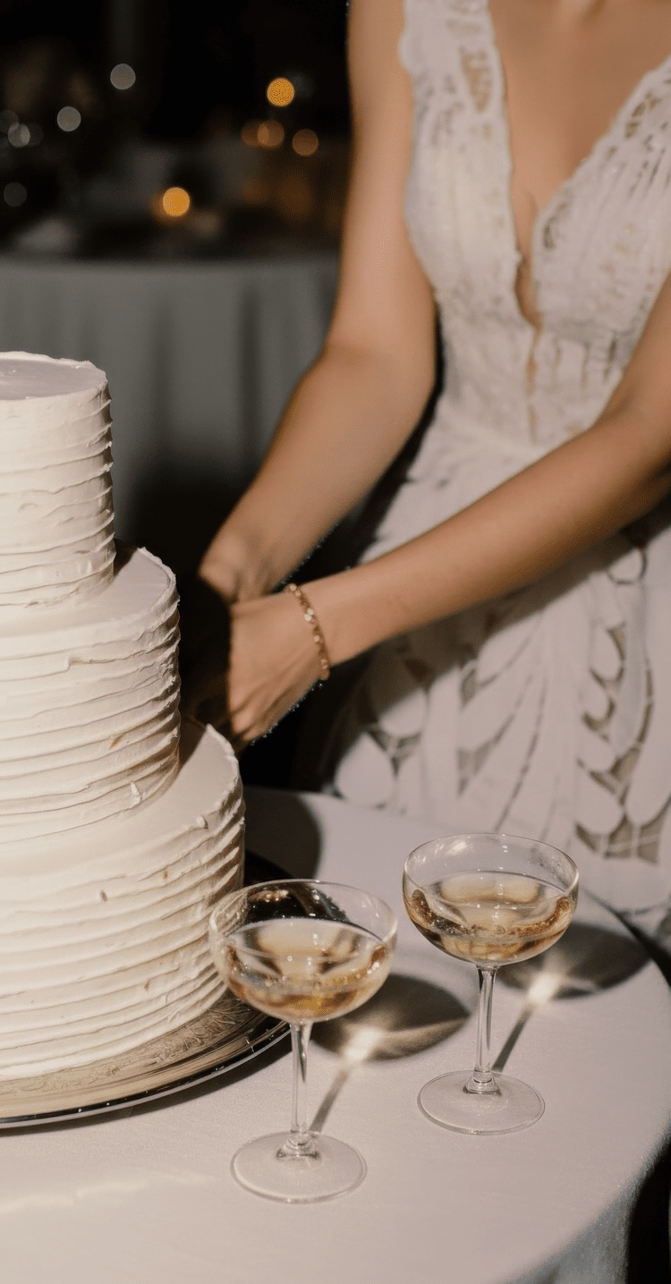 A woman in a white dress is cutting a wedding cake, with two glasses of champagne on the table.