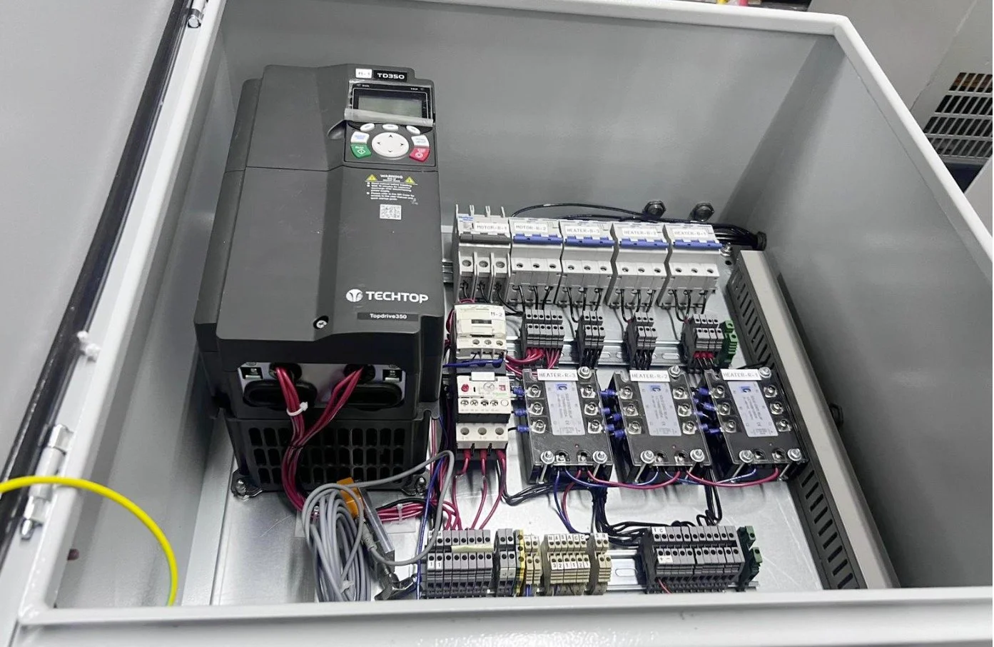 Electrical control panel with a black power supply unit, circuit breakers, relays, and wiring inside a metal enclosure.