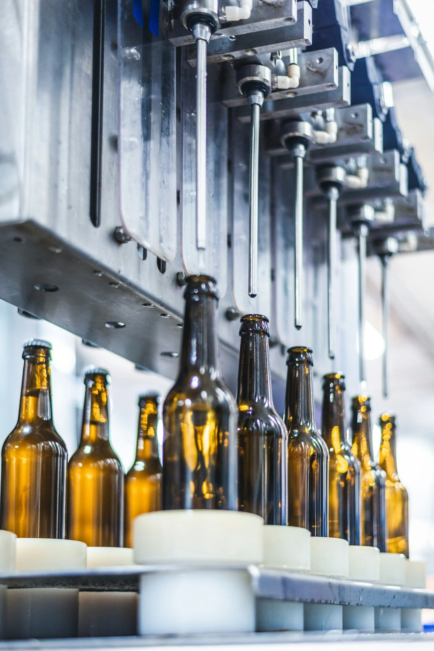 Glass bottles are being filled with liquid from a filling machine in a manufacturing or bottling plant.