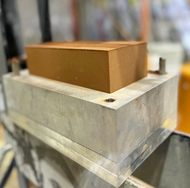 Close-up of a metal mold with a rectangular, brown rubber block placed inside.