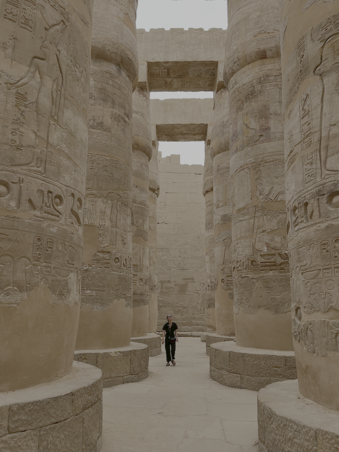 An ancient Egyptian temple with large carved stone columns inscribed with hieroglyphics, and a person walking through the site.