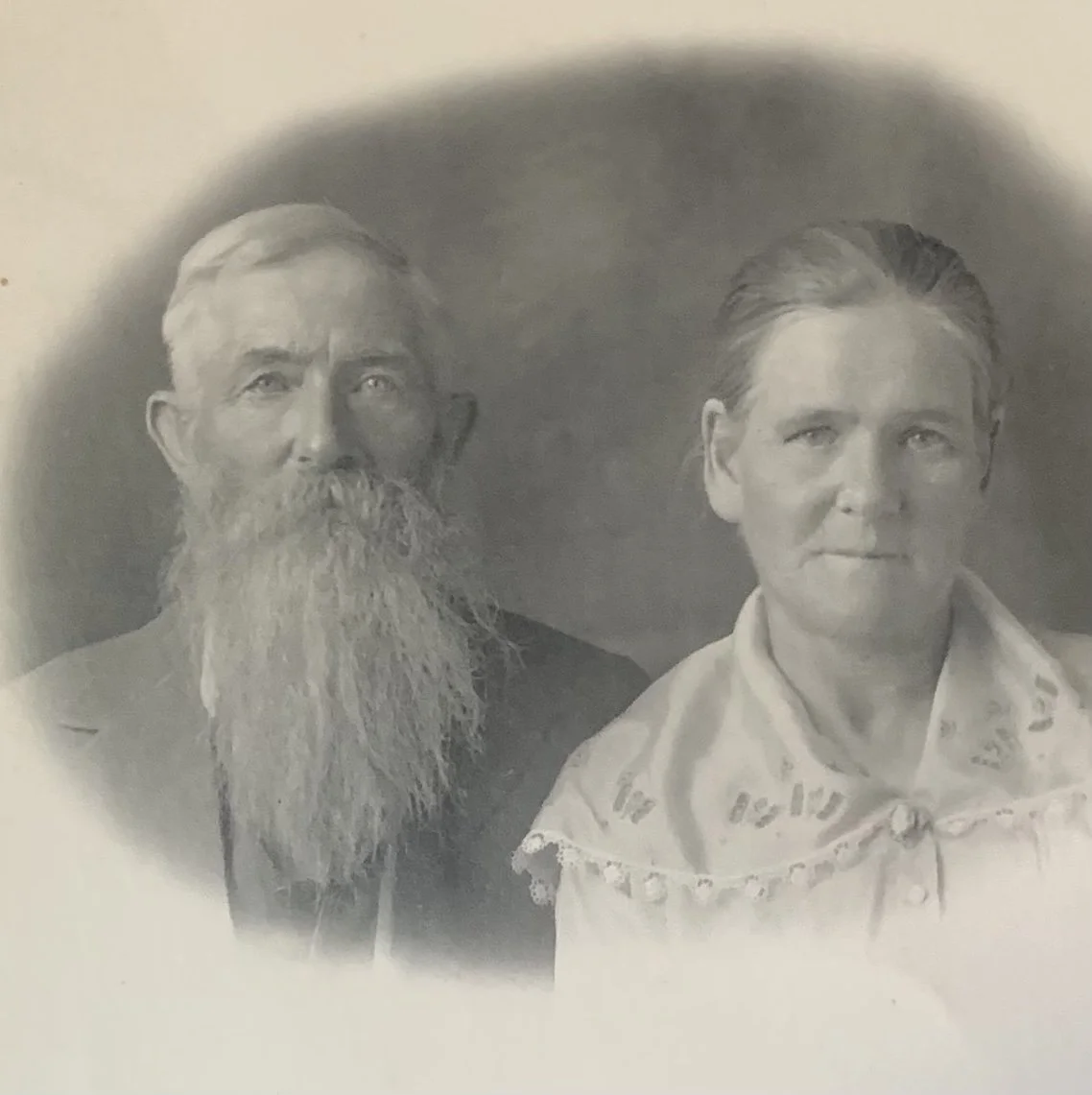 A black and white photo of a bearded man with a serious expression and a woman with a neutral expression, both facing forward.