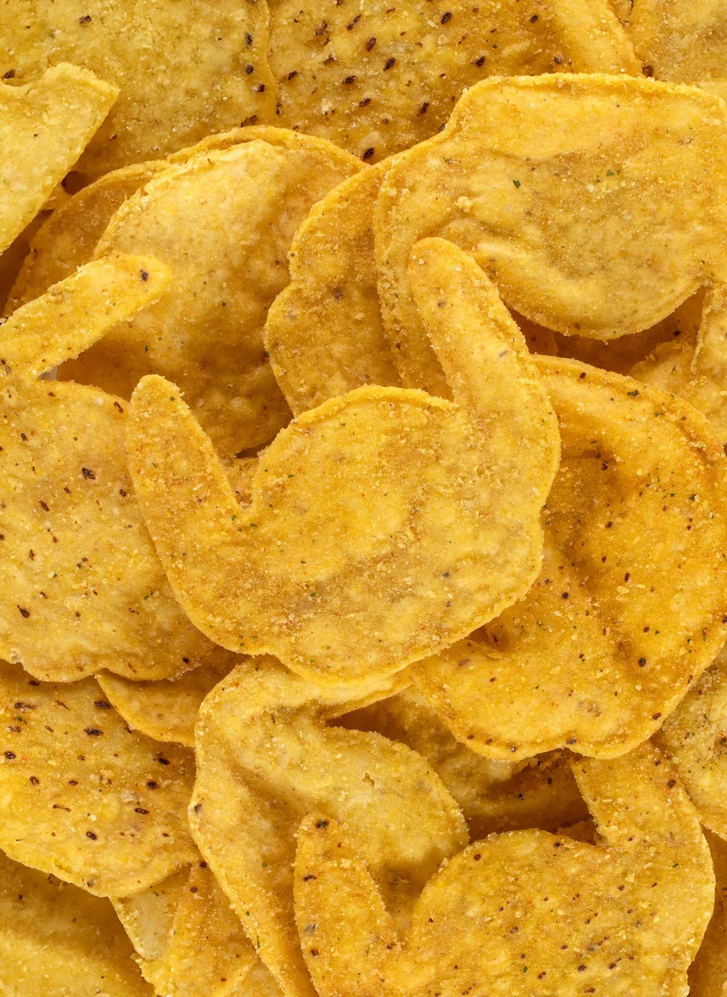 Close-up of seasoned tortilla chips with a yellow and orange hue, sprinkled with spices and herbs.
