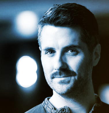 Black-and-white portrait of a man with short hair and a mustache, looking directly at the camera with a slight smile.