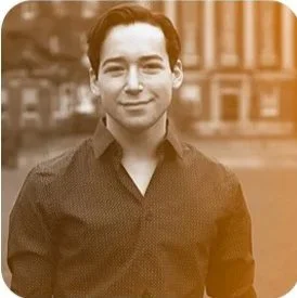 A young man smiling outdoors in front of a building, sepia tone.
