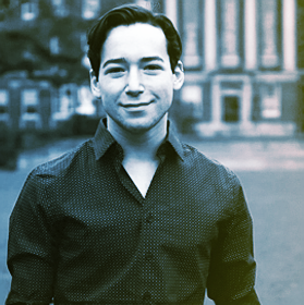A young man smiling outdoors in front of a building, sepia tone.