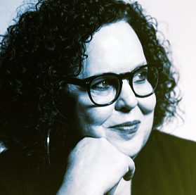 A woman with curly hair and glasses resting her chin on her hand, looking away thoughtfully.