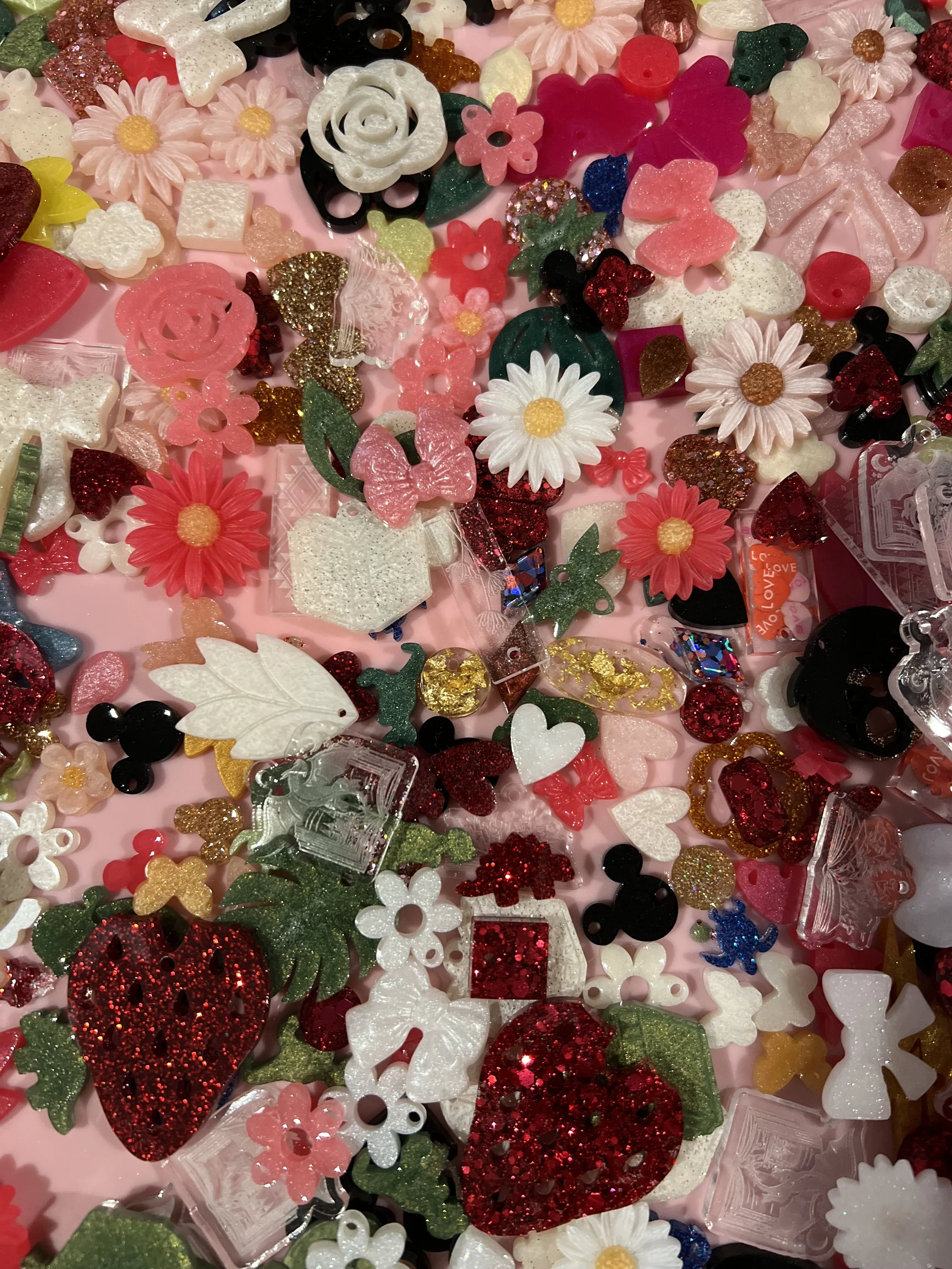 A collection of various colorful plastic and glittery decorative items including hearts, flowers, butterflies, and leaves scattered on a pink surface.