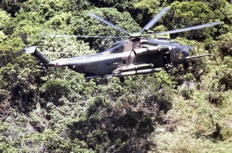 A HH-53C Super Jolly Green Giant helicopter flying over forested area.