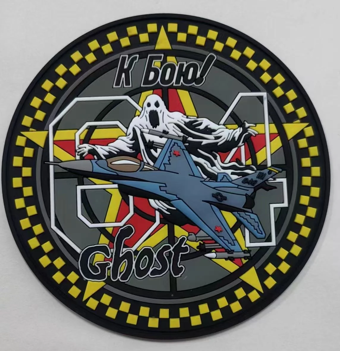 A circular patch with a checkered yellow and black border, featuring a ghost figure with an open mouth, a military jet, and Cyrillic and Latin text reading 'К БОЮ!' and 'Ghost'.