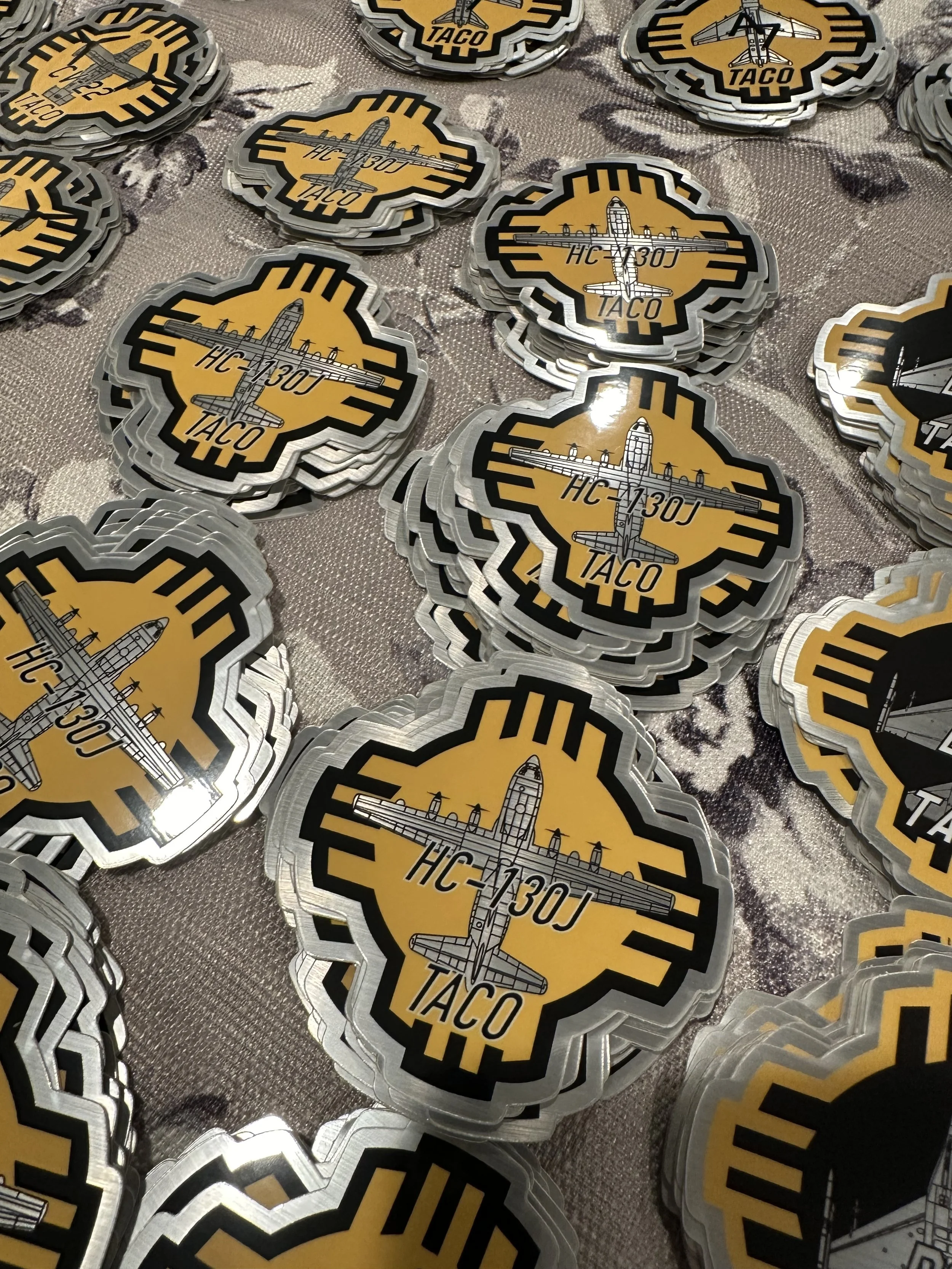 Multiple stickers featuring a plane illustration, the text HC-130J, and TACO on a gray textured surface.