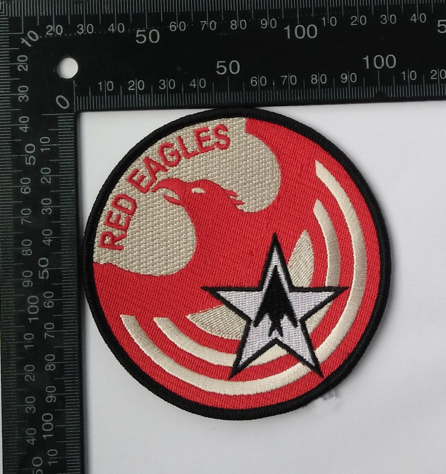 A circular embroidered patch featuring a black star with a white arrowhead inside it, a red eagle head, and the text "RED EAGLES" in red above the eagle, with concentric red and white rings beneath the star.