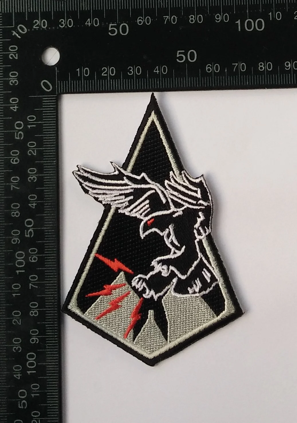 A patch featuring a black and gray design with a fierce bird and red lightning bolts, bordered by black.