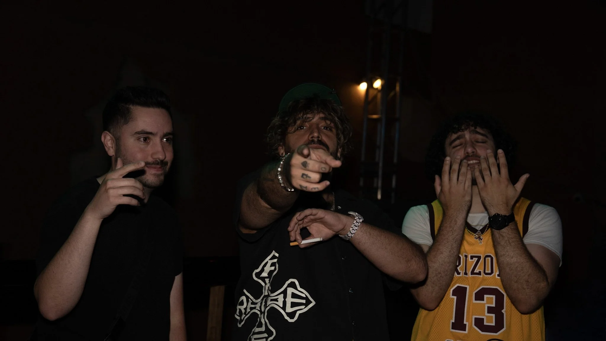 Concert Behind the Scenes (BTS) picture. Nightlife flash photography. Three men standing in a dark room, with the central figure pointing towards the camera.