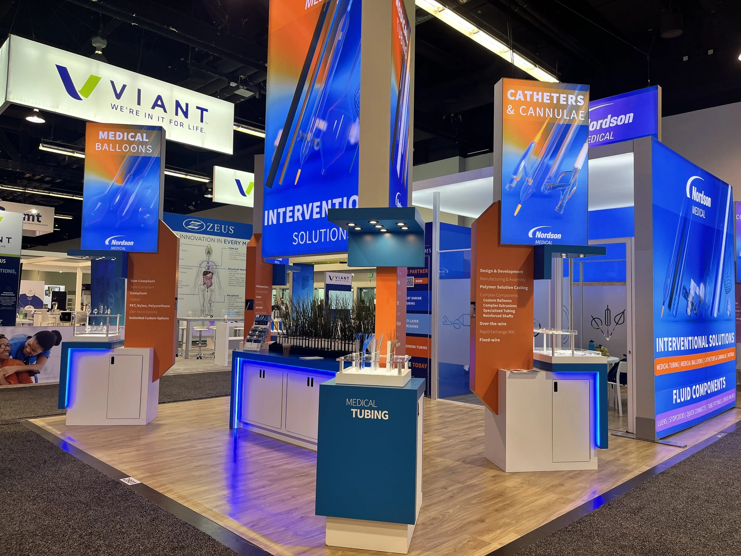 Booth at a medical trade show with colorful signs and banners displaying medical supplies such as catheters, cannulae, balloons, and tubing from Nordson MEDICAL.
