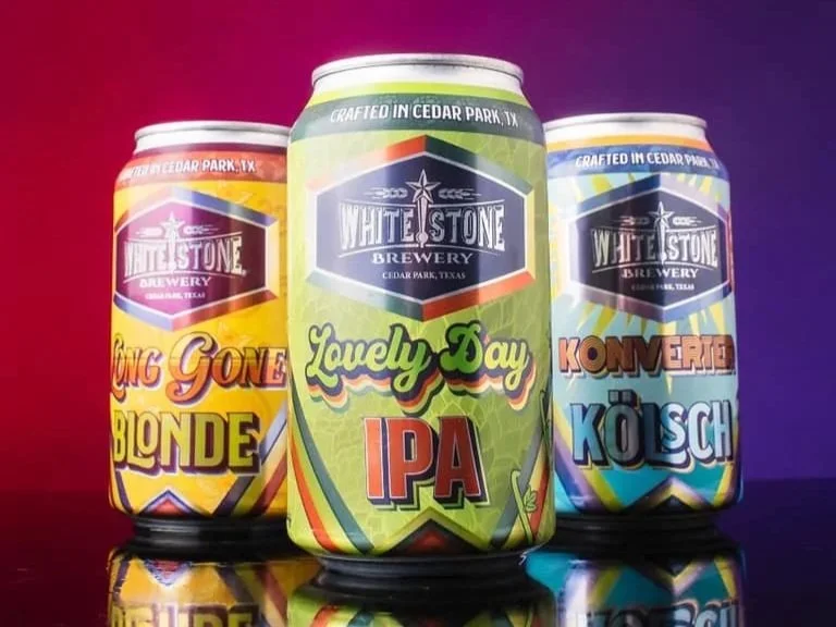 Three colorful cans of craft beer from Whitestone Brewery, with a purple and red background.