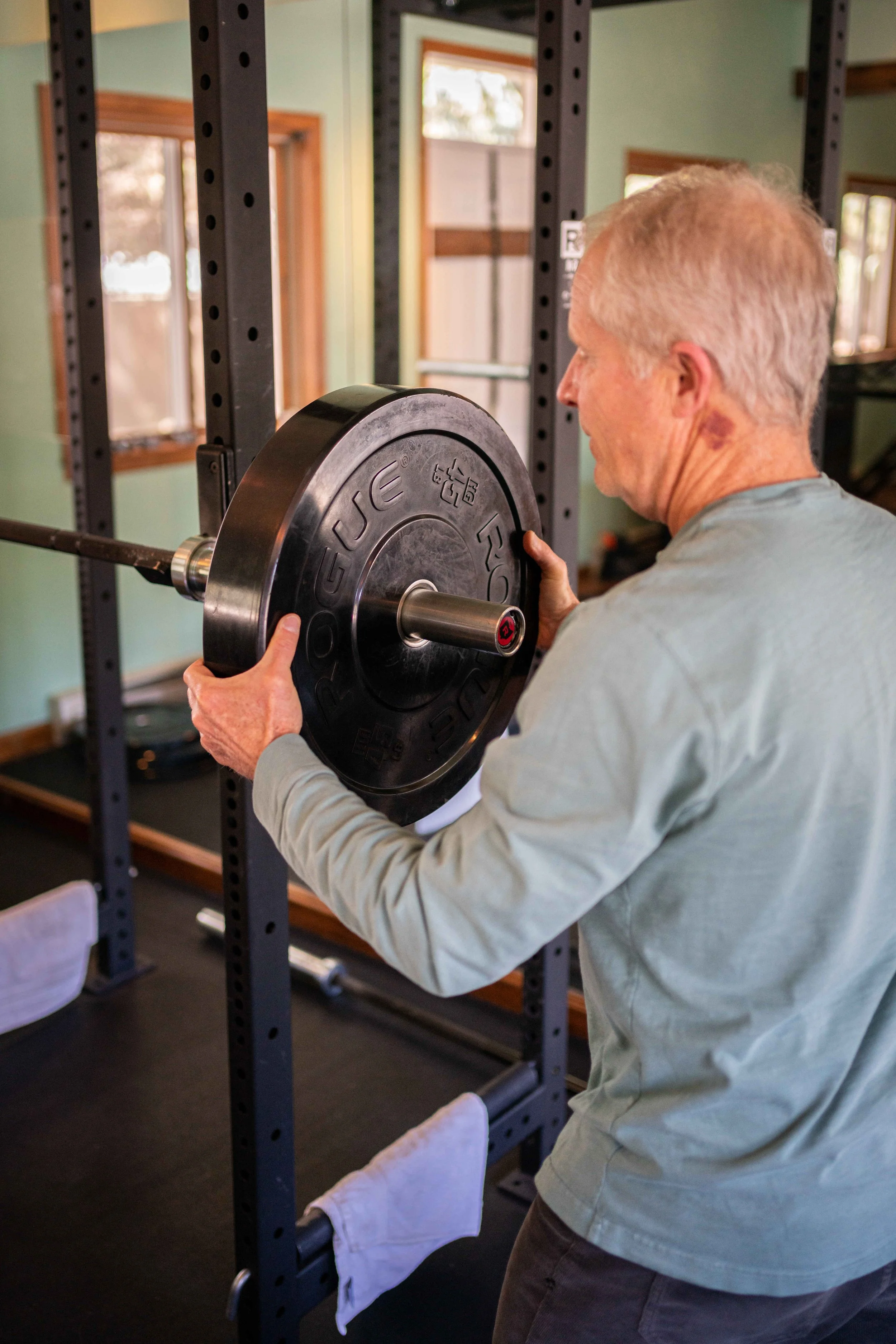 An elderly man lifting a heavy barbell with weight plates in a gym in Eagle, CO.