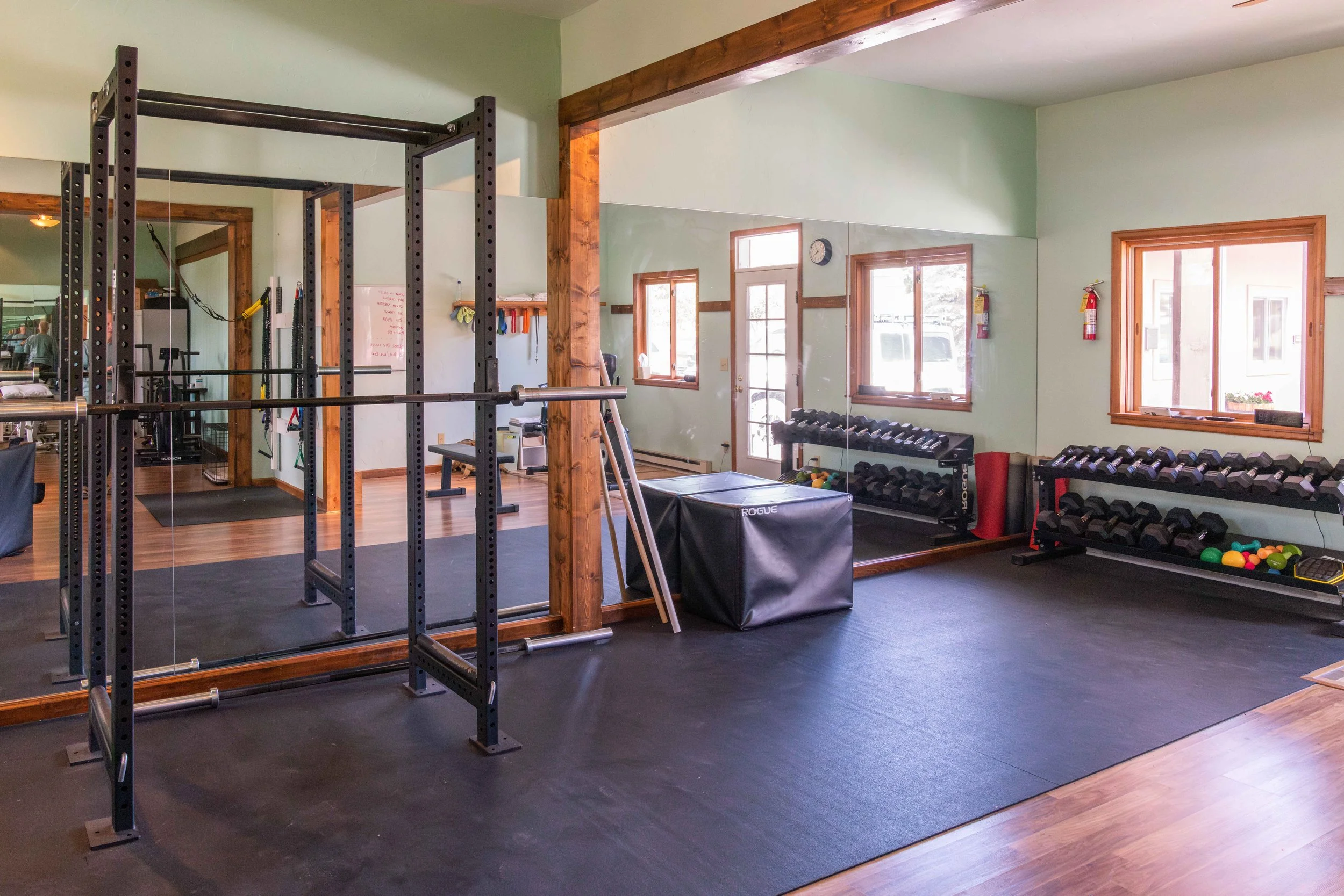 Physical therapy room and gym with weight racks, dumbbells, plyometric box, medicine balls, and a large mirror on the wall in Eagle, CO.