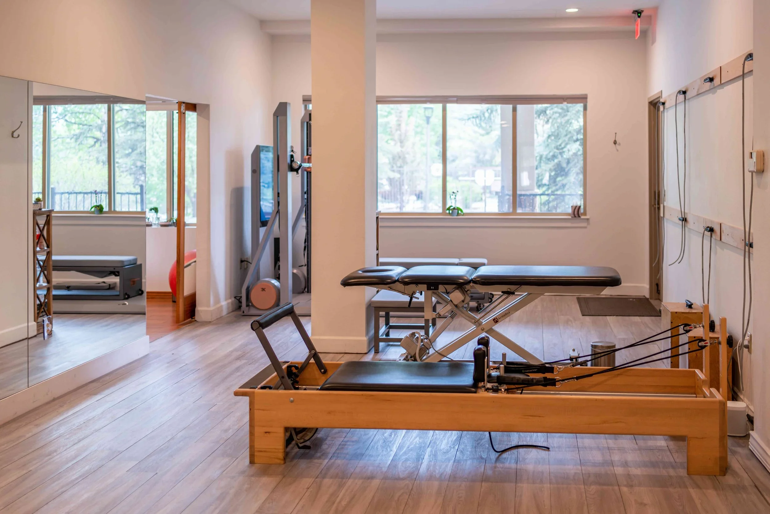A physical therapy and performance training room with a Pilates reformer, a massage table, squat rack and exercise equipment in Avon, CO.