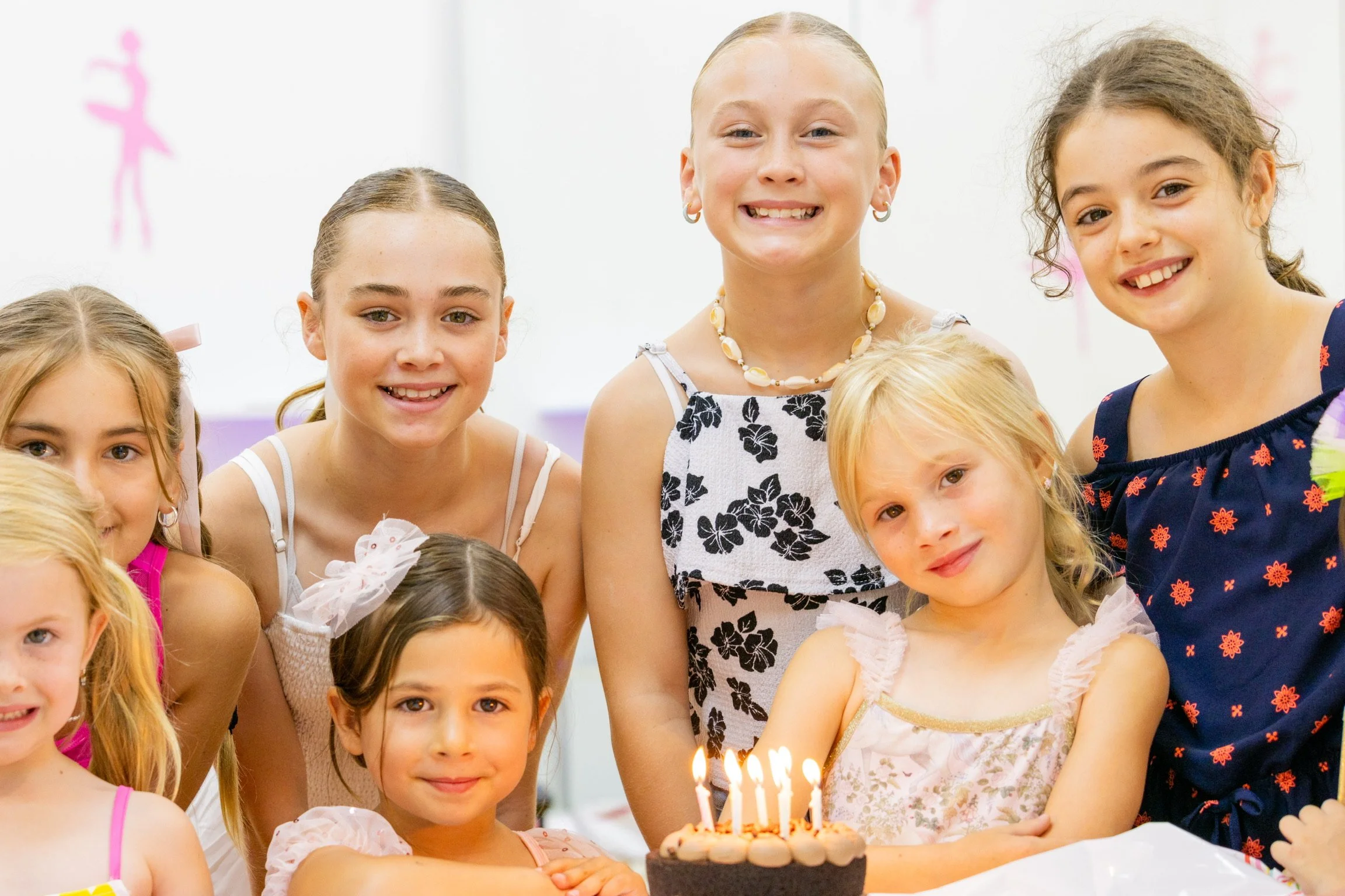 A group of girls celebrating a birthday with a chocolate cake topped with lit candles.