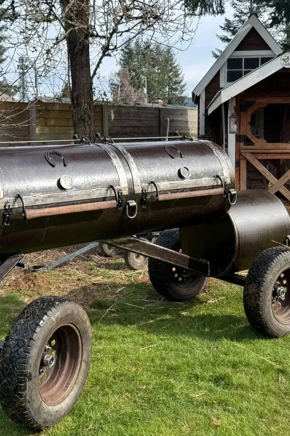 BBQ smoker with horseshoe embellishments on the front set in the grass in front of a red chicken coop.