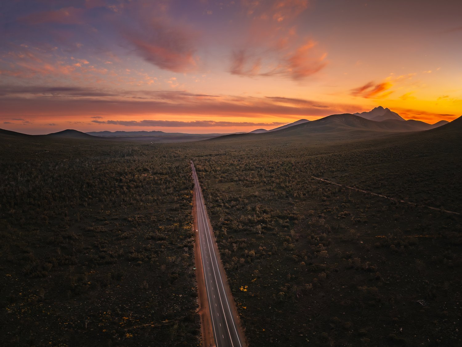 Aerial view of a road leading towards the Stirling Range beneath a dramatic sunset sky.