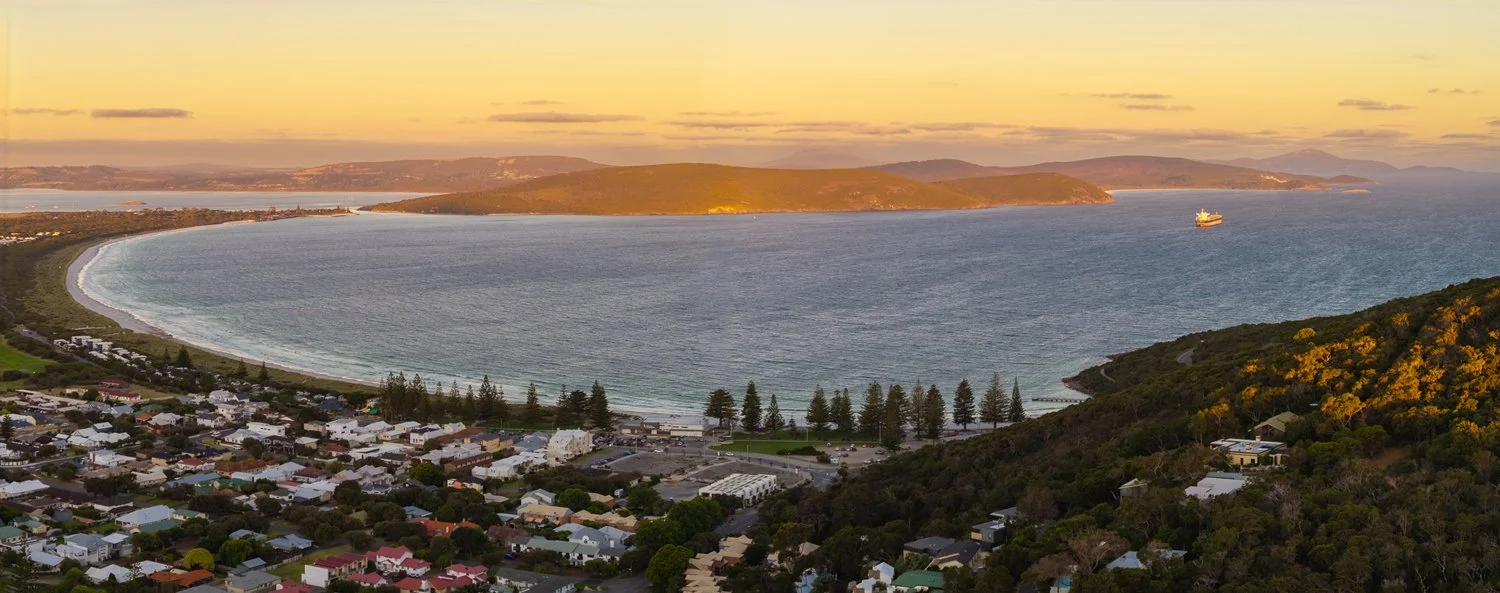 Elevated view across Albany's Middleton Beach coastline, harbour and surrounding hills in warm evening light.