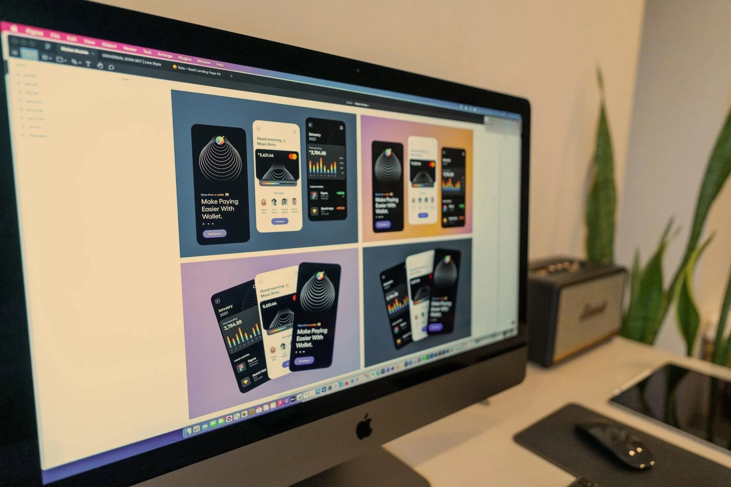 A computer screen displaying a graphic design project with mockups of mobile app interfaces for fitness and finance apps, on a cluttered desk with a mouse, a tablet, and some plants in the background.