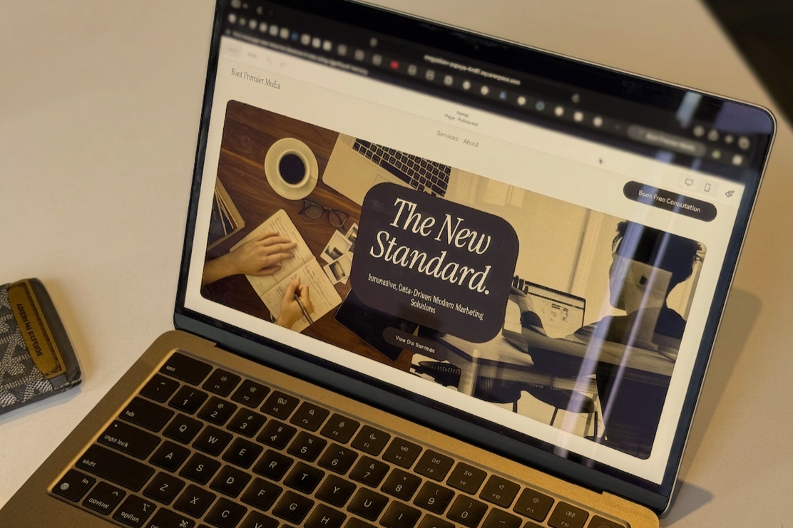 Laptop displaying a website, with a coffee cup, glasses, and a book on the desk