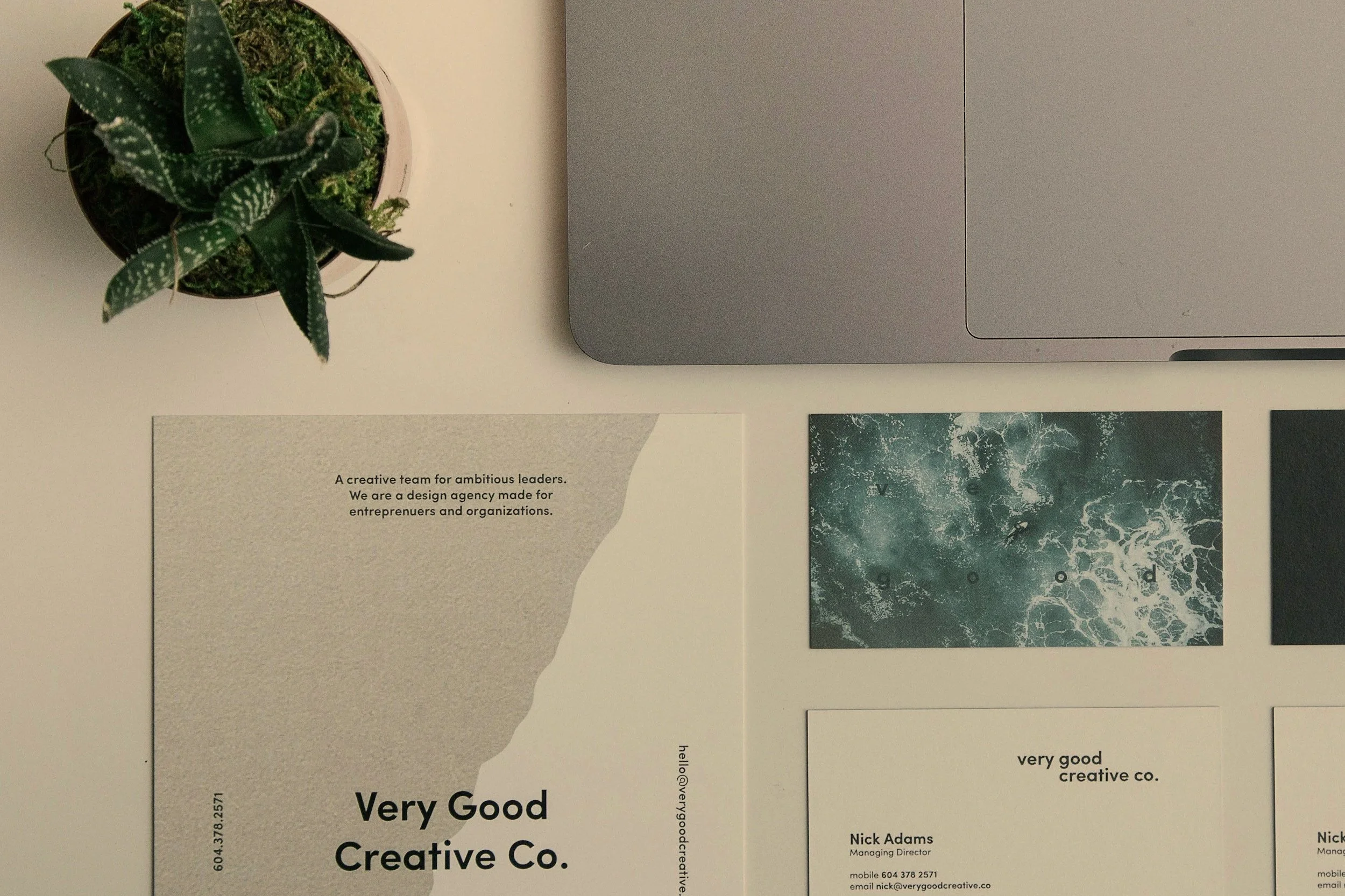 Top view of a workspace with a potted plant, a laptop, and several printed promotional materials for Very Good Creative Co.