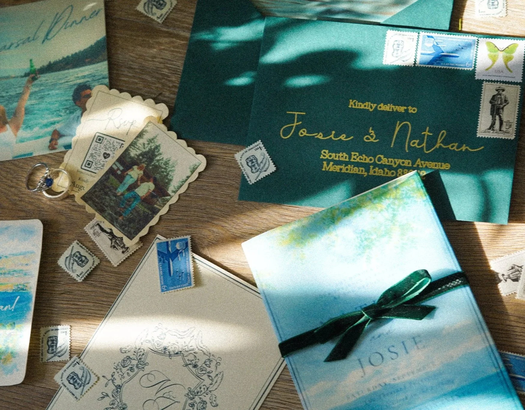 A collection of letters, postcards, postage stamps, and rings on a wooden surface, with a teal-colored envelope addressed to Josie and Nathan.